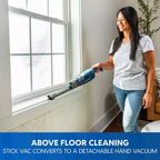 Woman using a stick vacuum to clean above a window